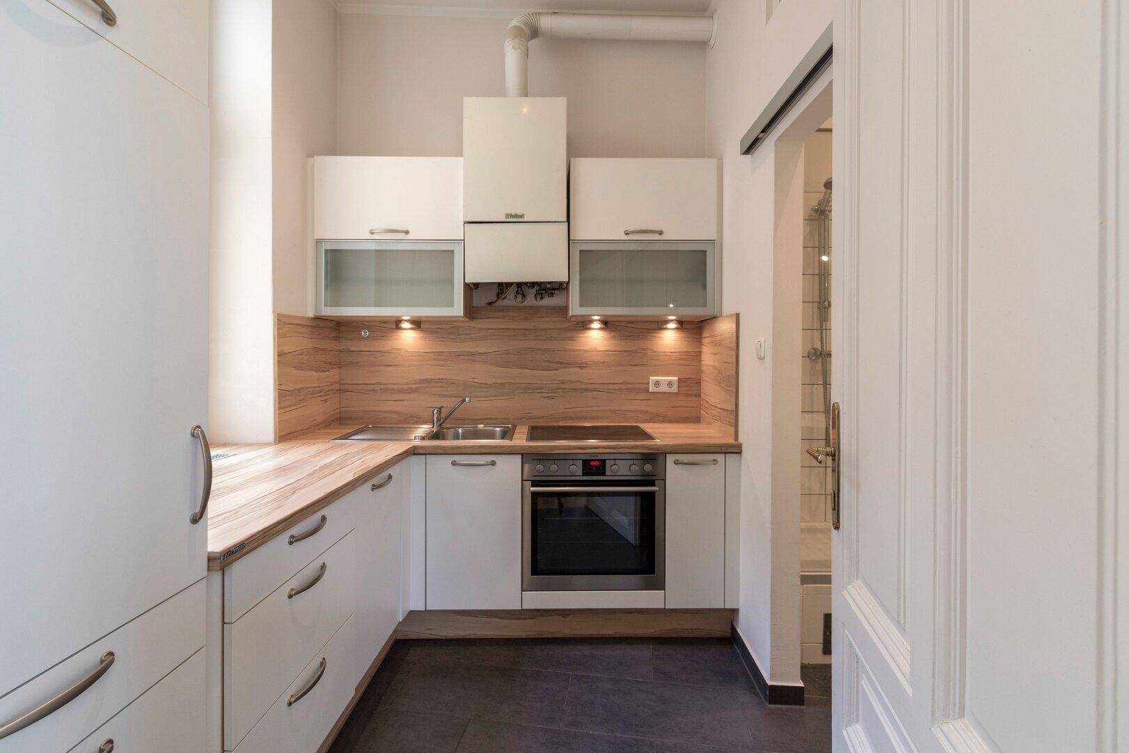 Moderne Einbauküche mit weißen Schränken, Holzoptik-Arbeitsplatten und integrierten Geräten.
