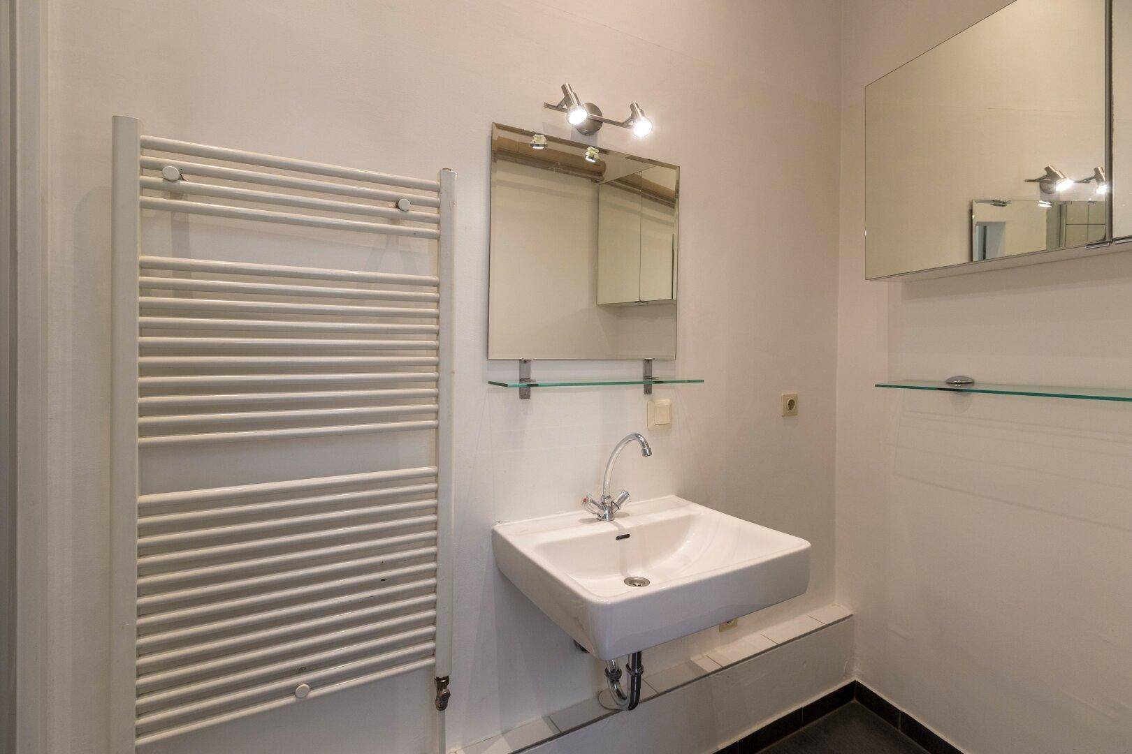 Funktionales Badezimmer mit Waschbecken, Spiegel und praktischem beheiztem Handtuchhalter.