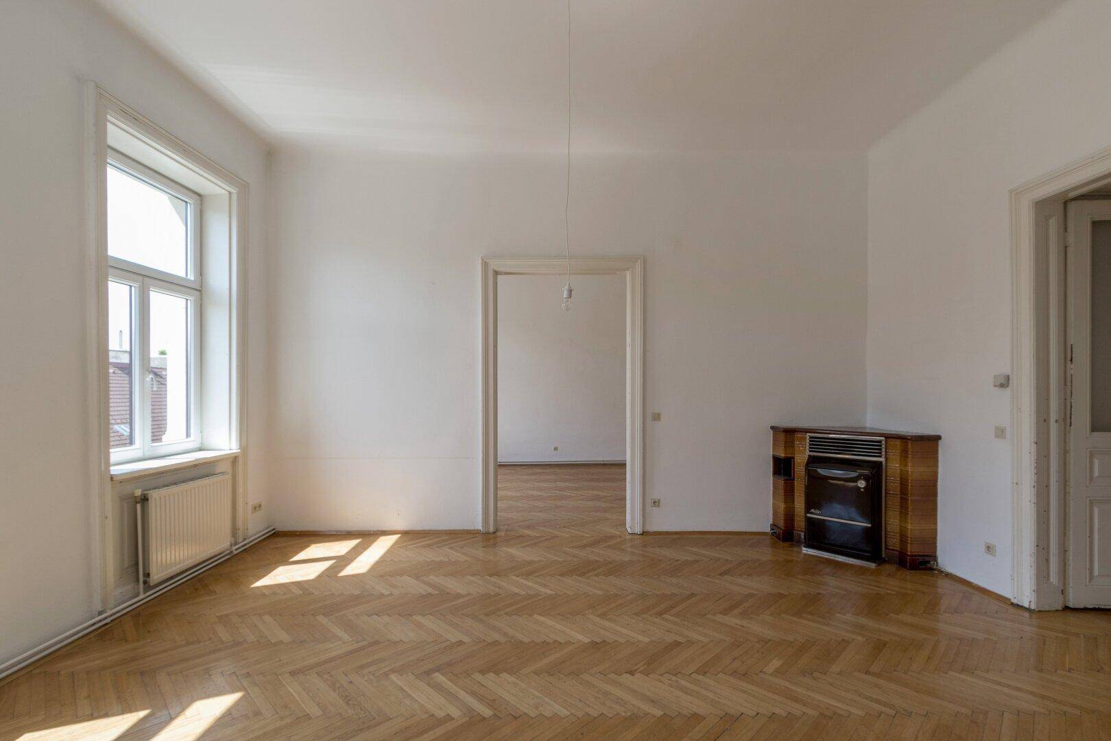 Großes, helles Zimmer mit Fischgrätparkett und einem dekorativen Ofen.