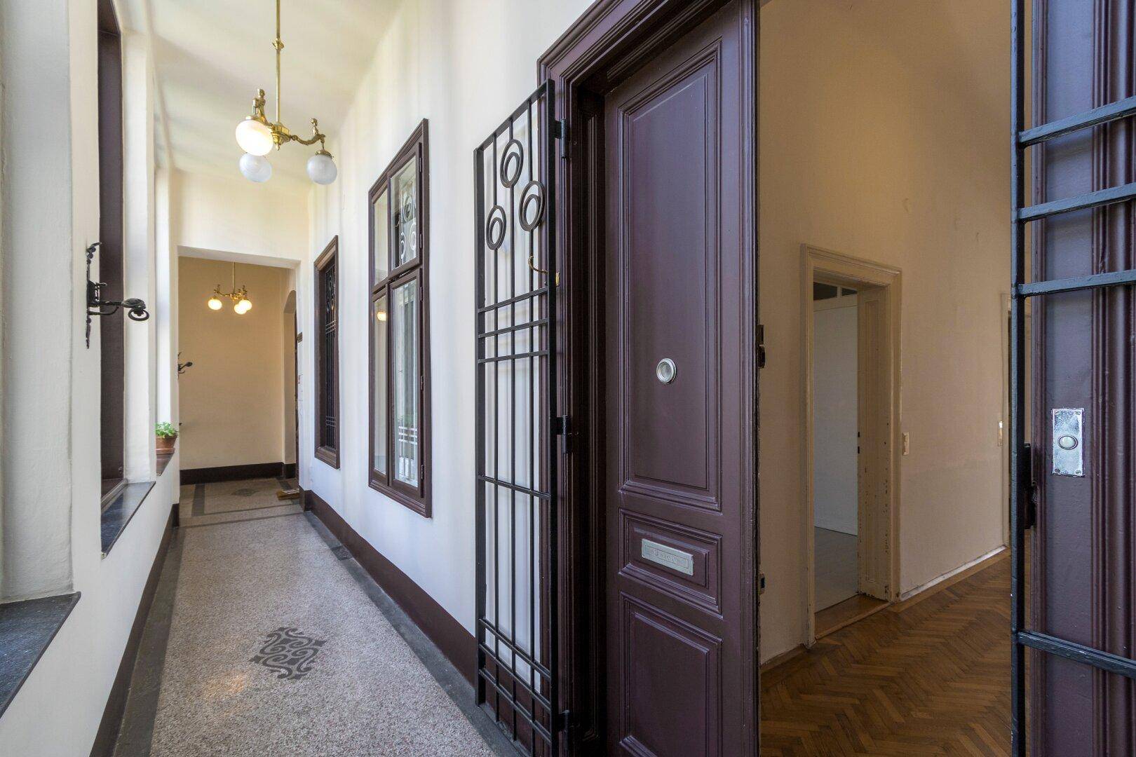 Historischer Flur mit Terrazzoboden, hohen Decken und dekorativen Elementen.