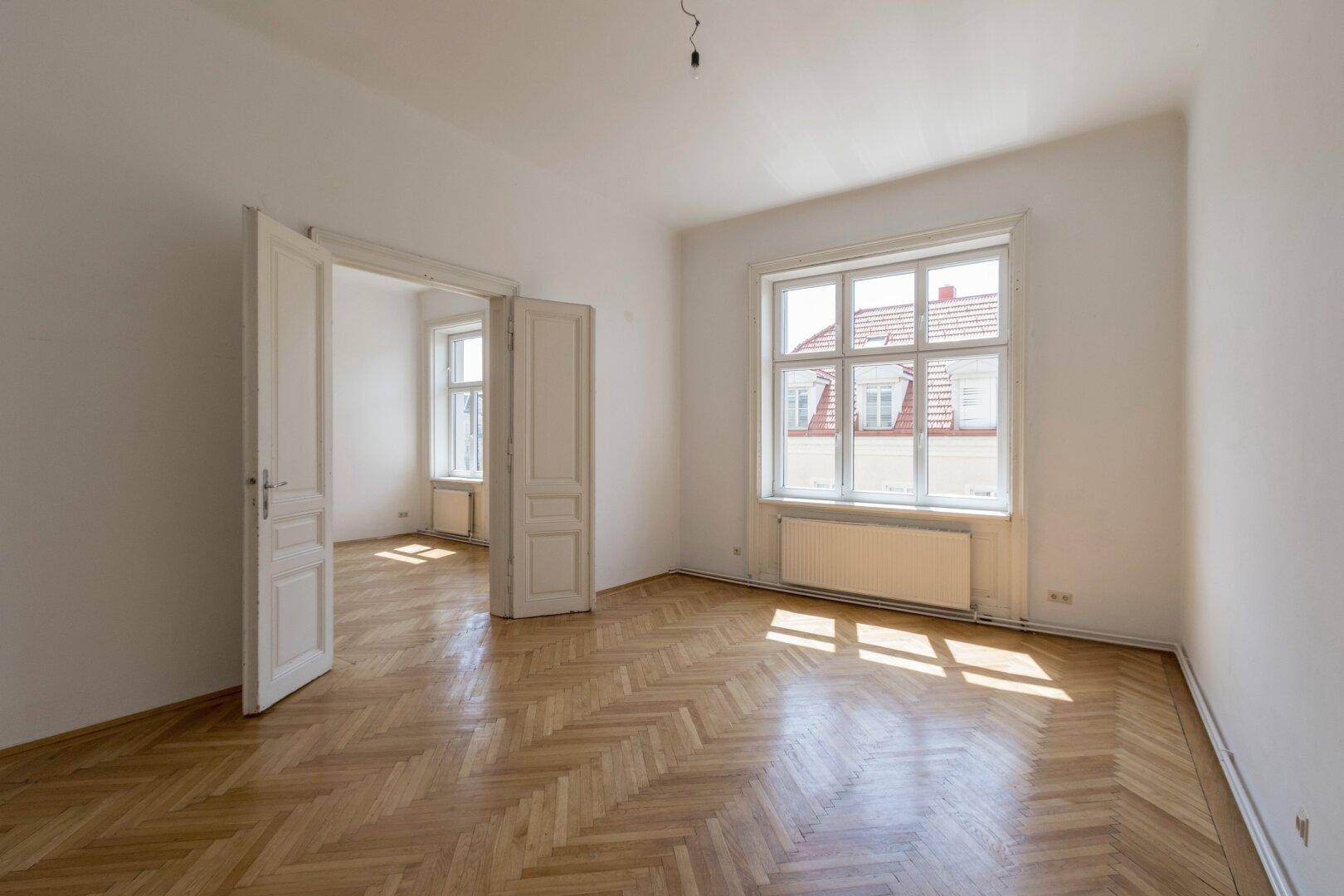 Geräumiges Zimmer mit klassischem Fischgrätparkett und hohen Doppeltüren.
