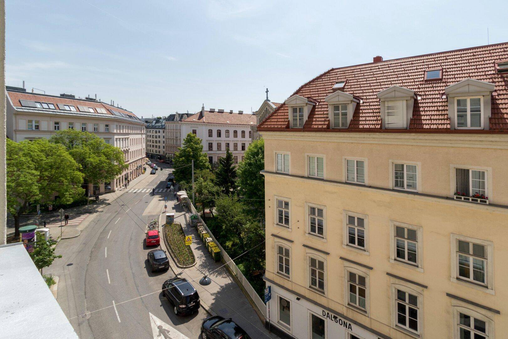 Blick von oben auf eine belebte Straße mit historischen Gebäuden und Bäumen.