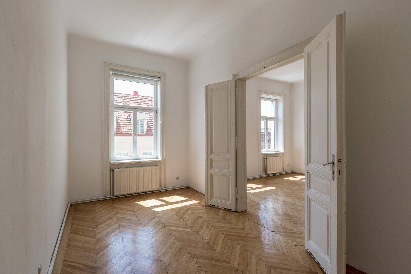 Heller Raum mit Fischgrätparkett und Blick auf die umliegenden Gebäude.