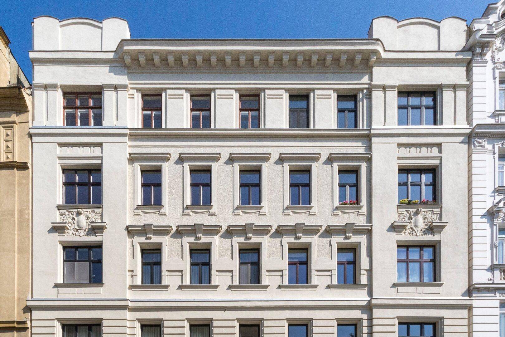 Klassische Altbaufassade mit vielen Fenstern und dekorativen Elementen unter blauem Himmel.