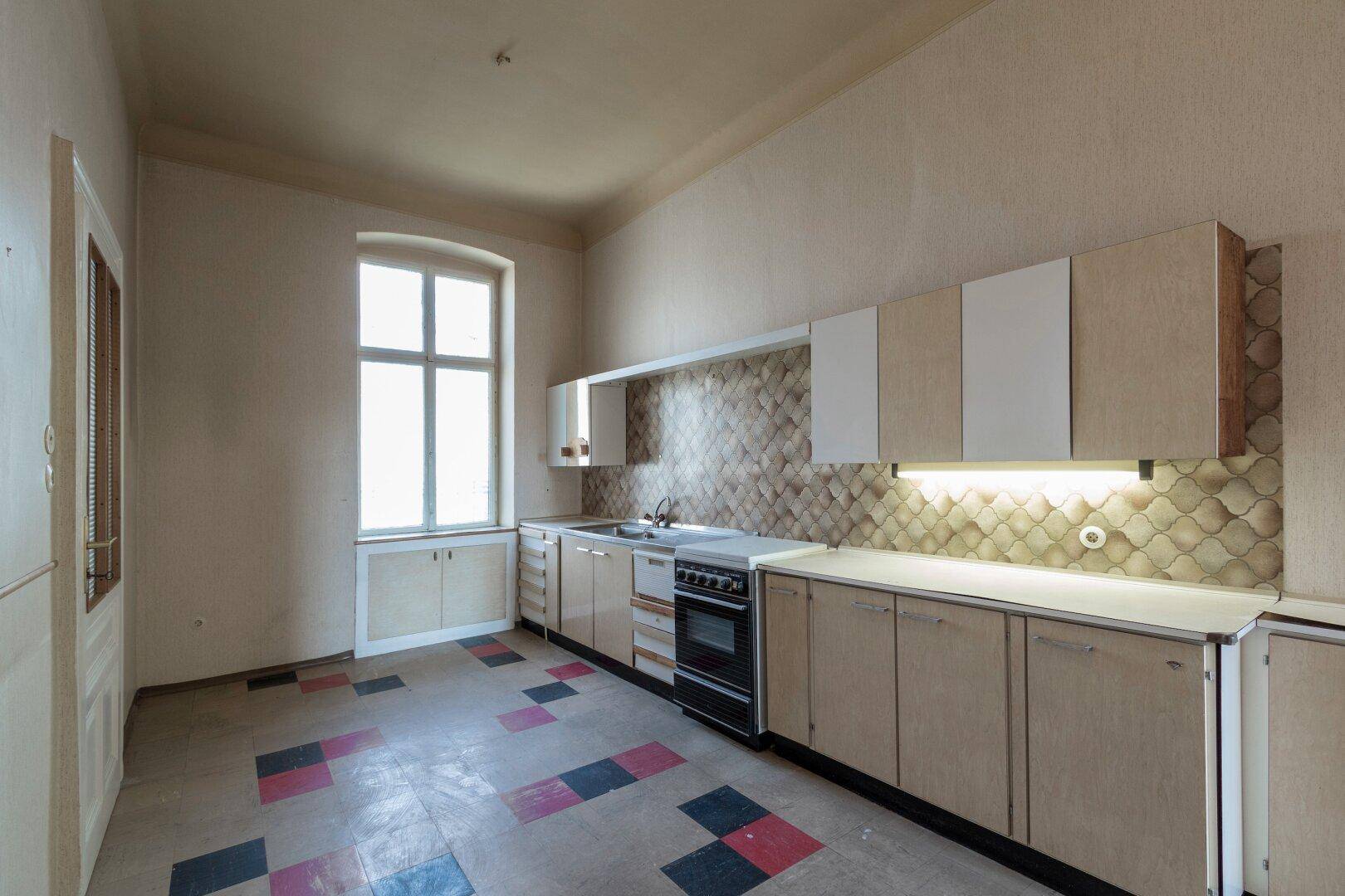 Küche im Vintage-Stil mit älteren Einbaumöbeln und farbigen Fliesenboden, bereit zur Modernisierung.