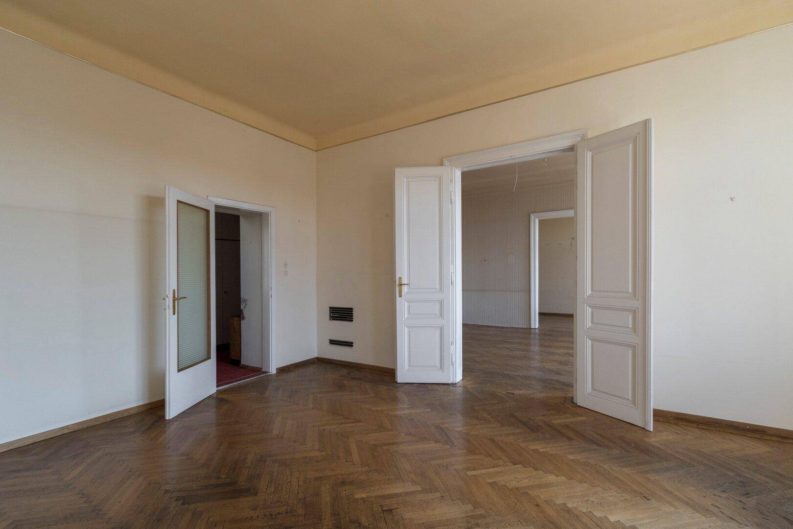 Geräumiges Zimmer mit Fischgrätparkett und Zugang zu anderen Räumen, ideal für eine offene Gestaltung.