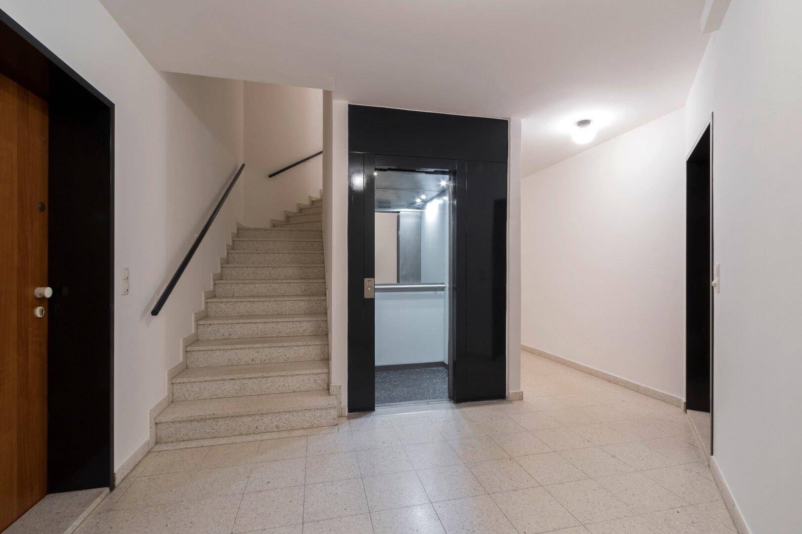 Heller Eingangsbereich mit Treppenhaus und modernem Aufzug für bequemen Zugang zu den Etagen.