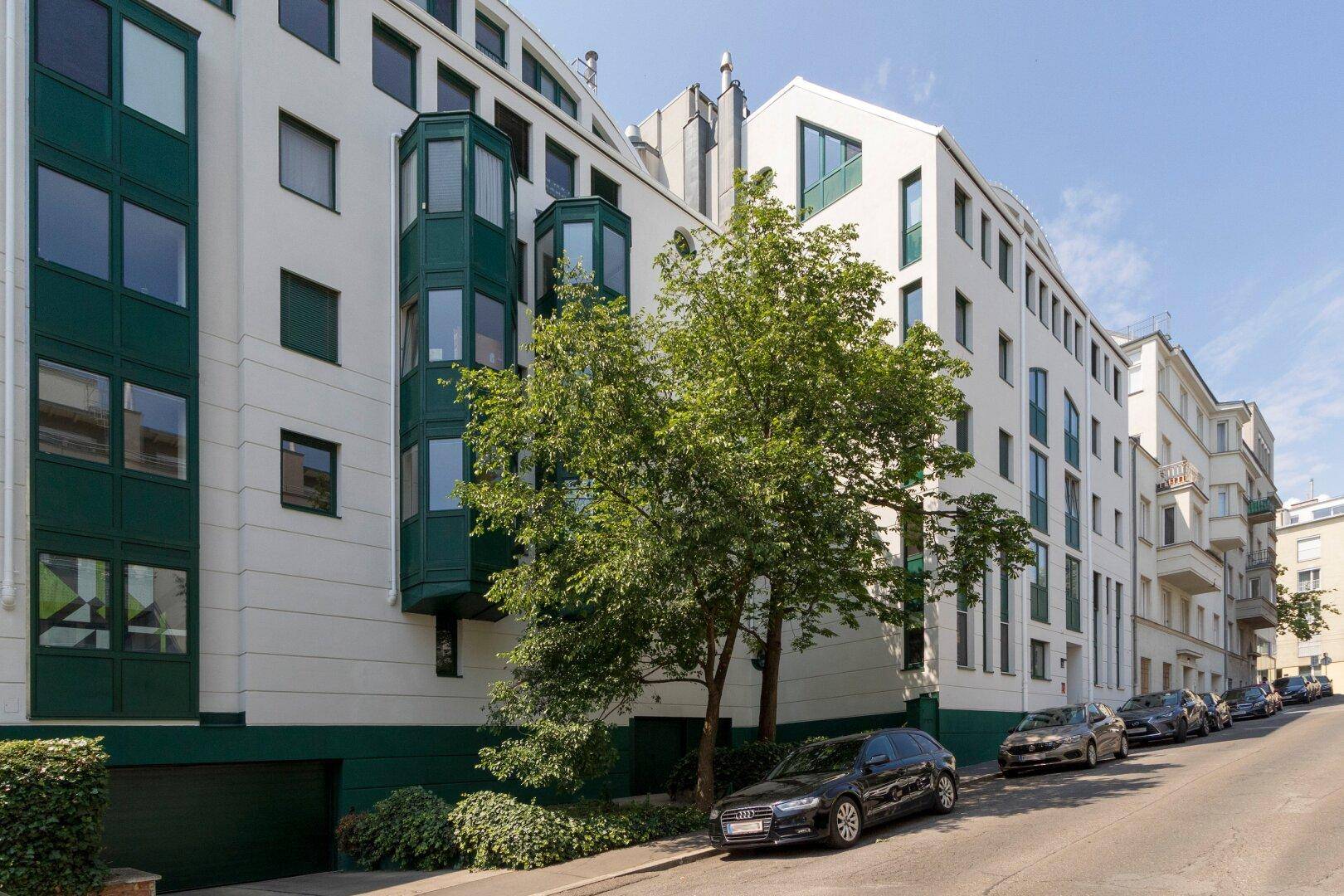 Ansicht des Gebäudes von der Straße mit grünen Erkern und geparkten Autos.