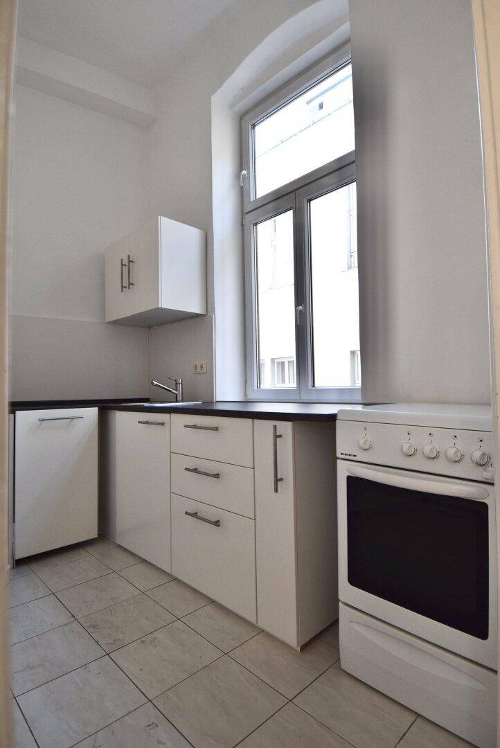 Kleine Küche mit weißen Schränken, schwarzer Arbeitsplatte und Fenster.
