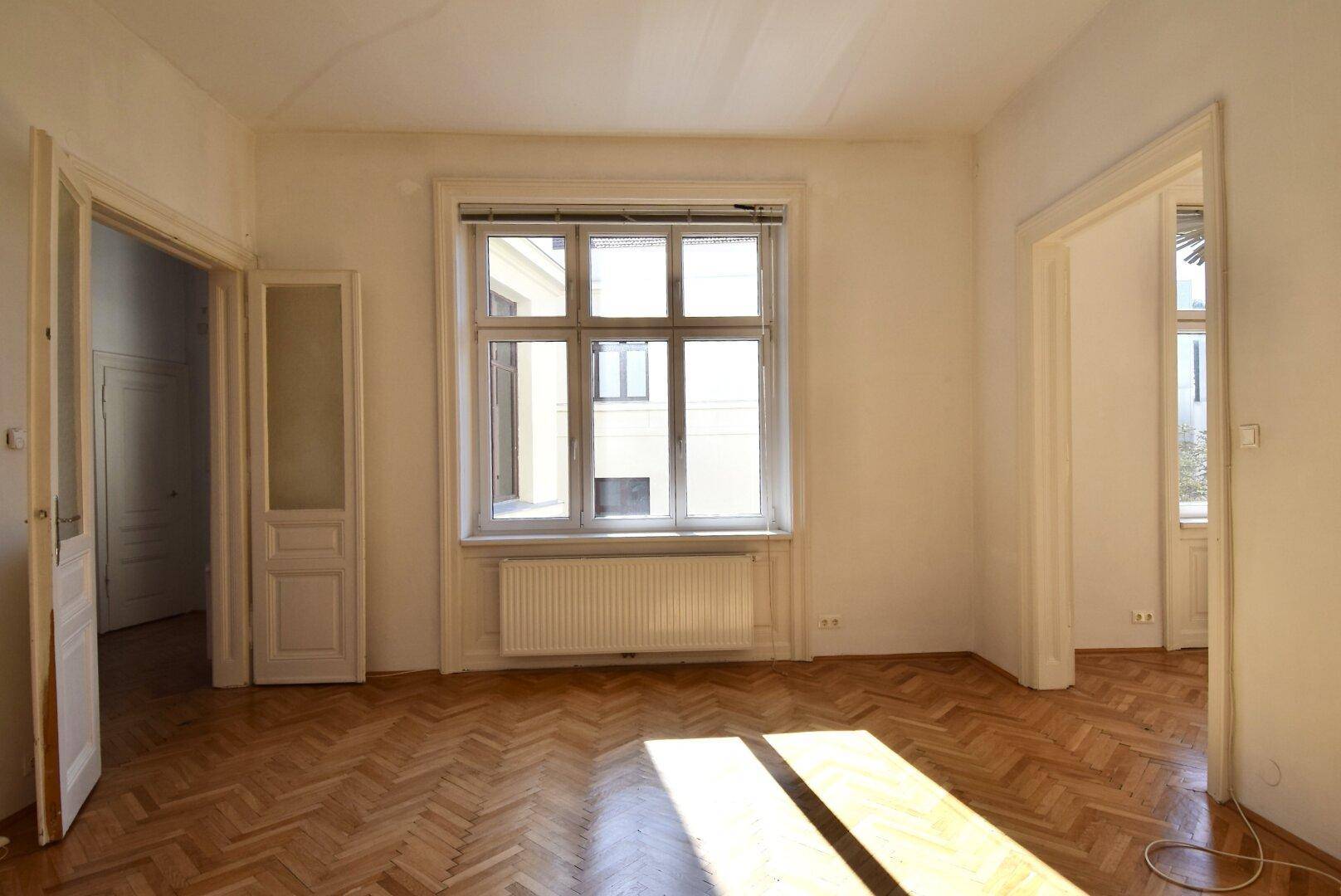 Lichtdurchflutetes Zimmer mit Fischgrätparkett und hohen Decken in einem Altbau.