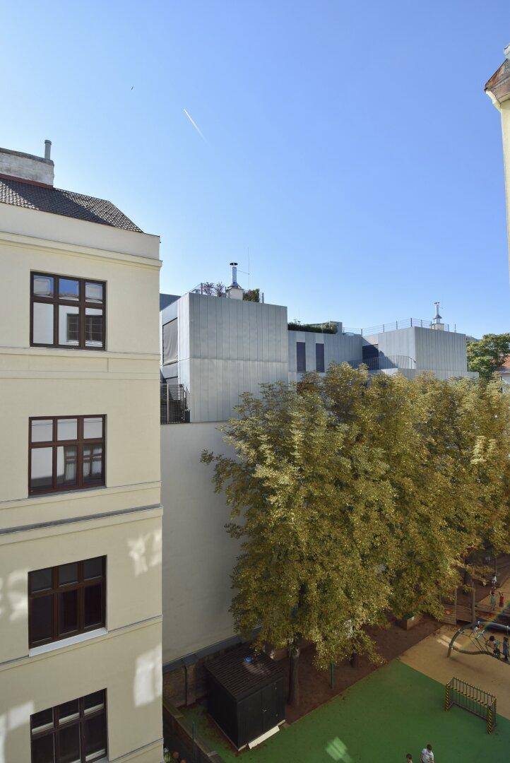 Blick aus dem Fenster auf einen begrünten Innenhof und umliegende Gebäude.