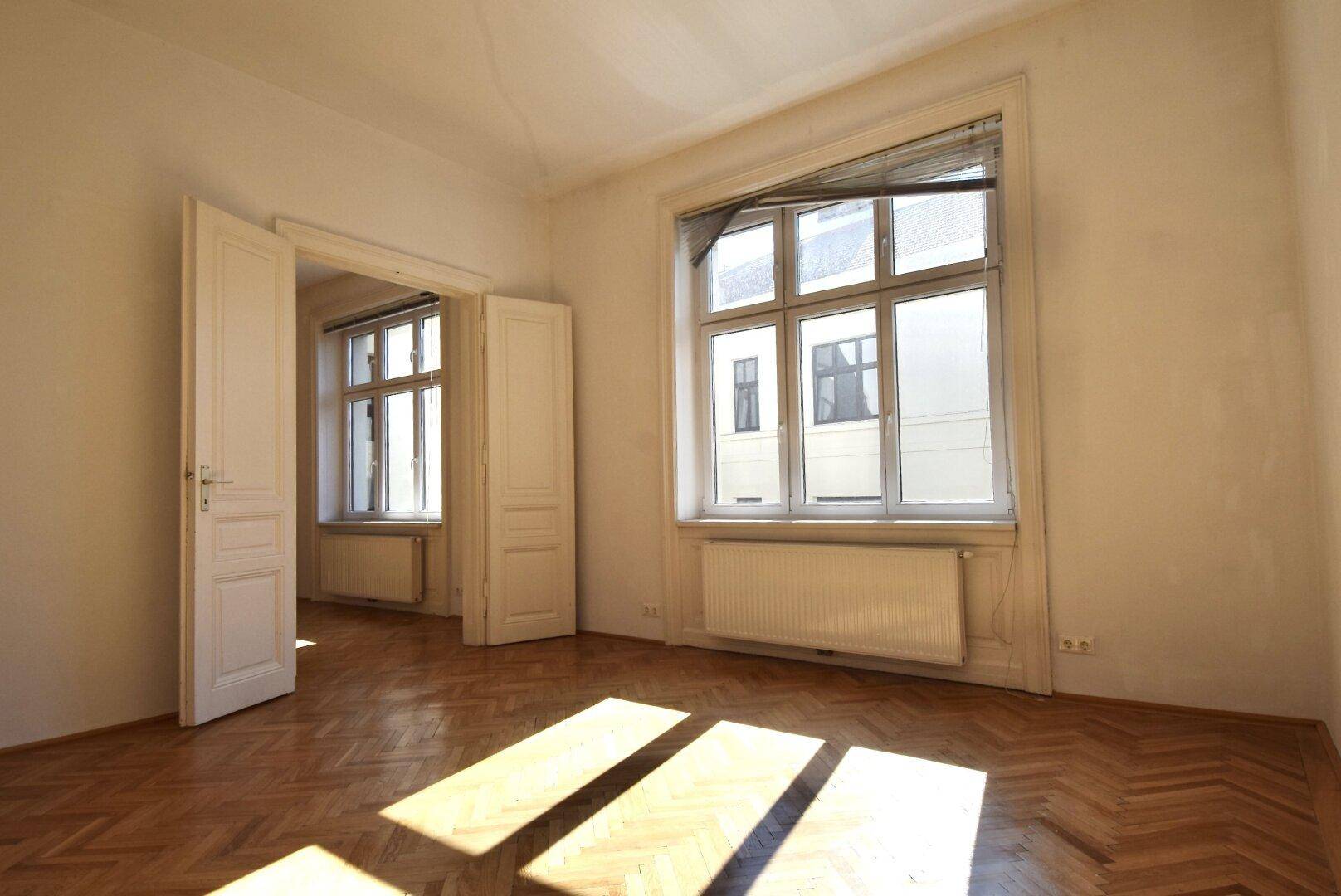 Geräumiges Zimmer mit klassischem Fischgrätparkett und sonnigem Lichteinfall.
