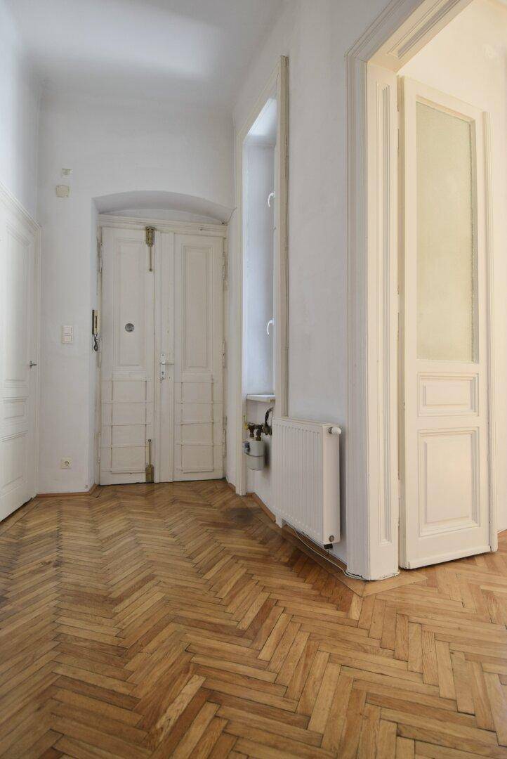 Flur mit Fischgrätparkett und historischen Türen, die den Altbaucharakter betonen.