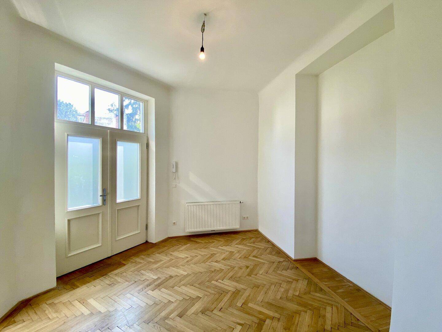 Eingangsbereich mit Fischgrätparkett, weißer Doppeltür und Heizkörper unter dem Fenster.