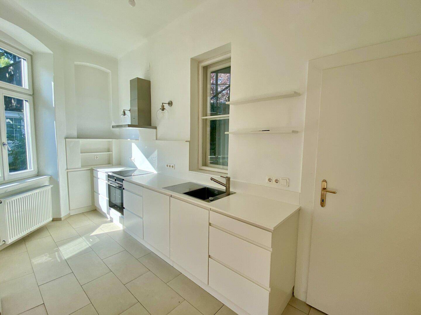 Moderne, helle Küche mit weißen Schränken, Einbaugeräten und Fenster mit Blick ins Grüne.
