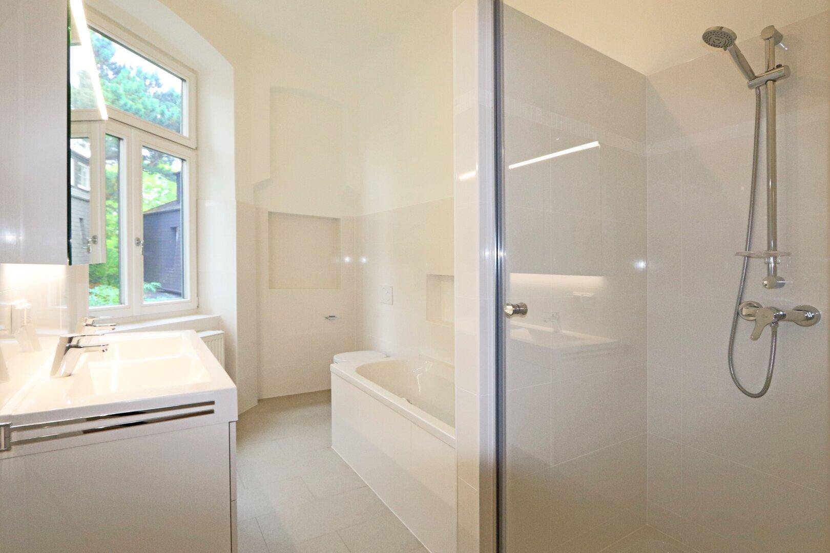 Modernes Badezimmer mit Badewanne, Dusche, Waschtisch und Fenster für Tageslicht.
