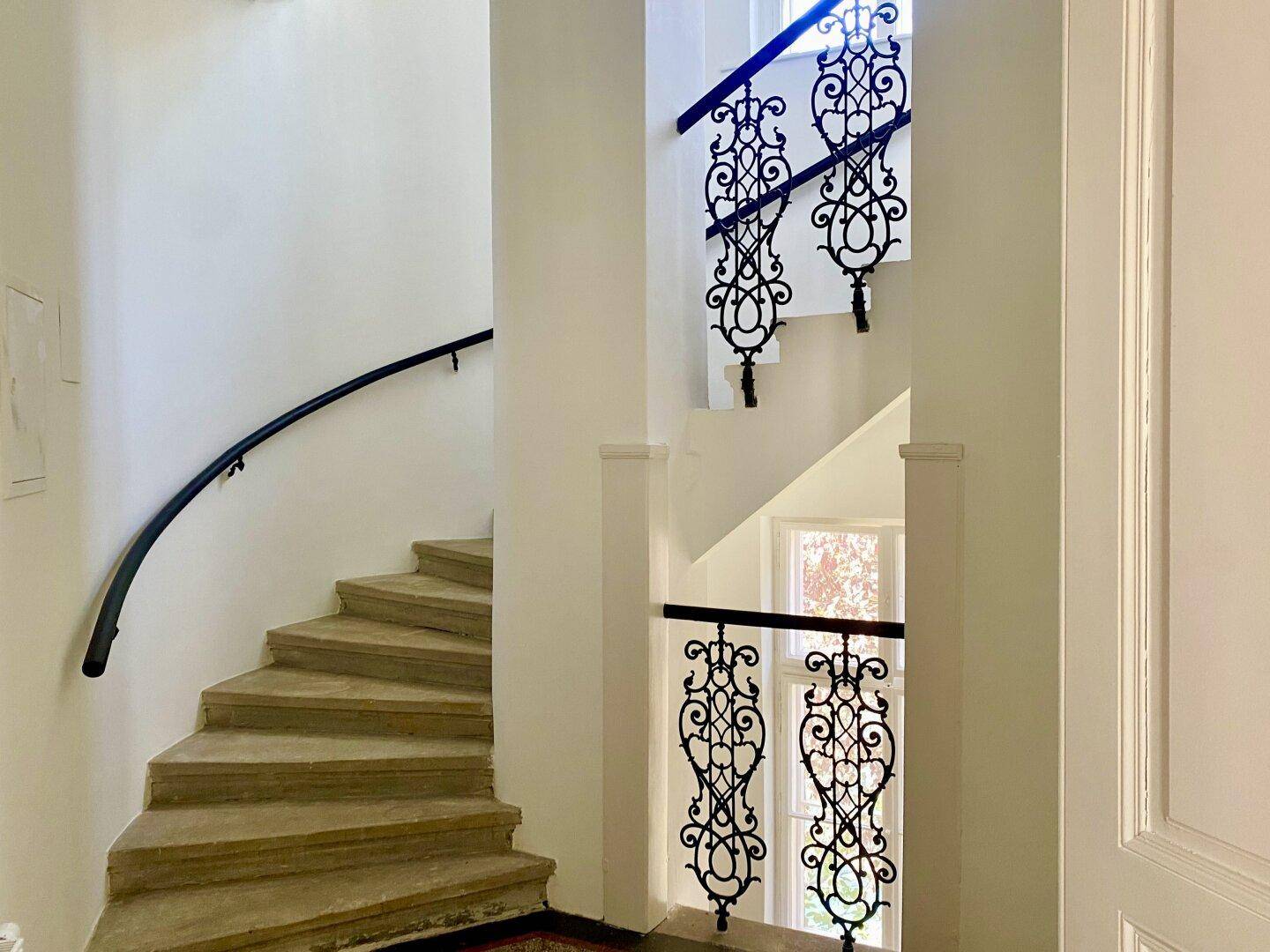 Elegantes Treppenhaus mit geschwungener Steintreppe und kunstvollen schmiedeeisernen Geländern.