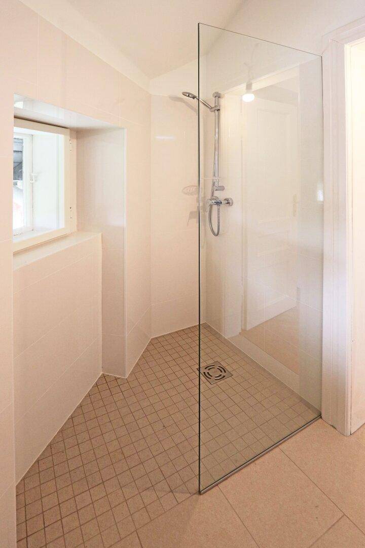 Modernes Badezimmer mit ebenerdiger Dusche, Fliesenboden und kleinem Fenster.