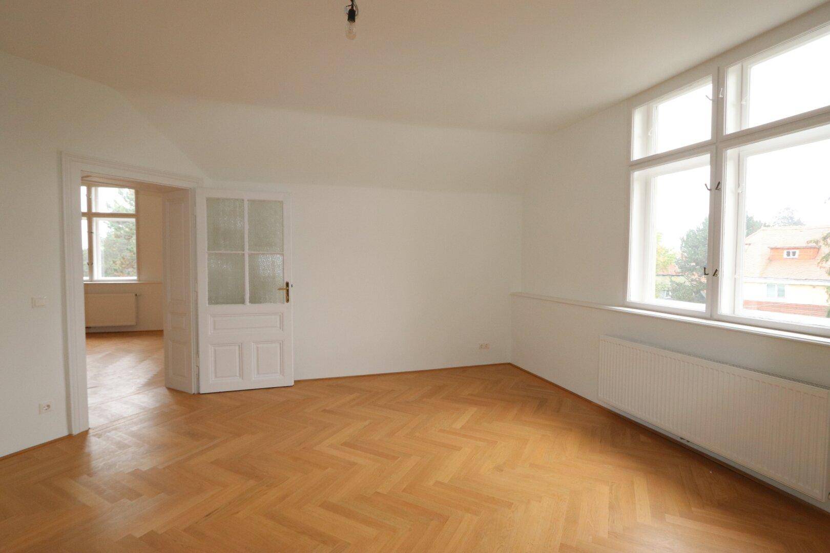 Heller Wohnraum mit Fischgrätparkett und großen Fenstern, die den Raum mit Licht füllen.