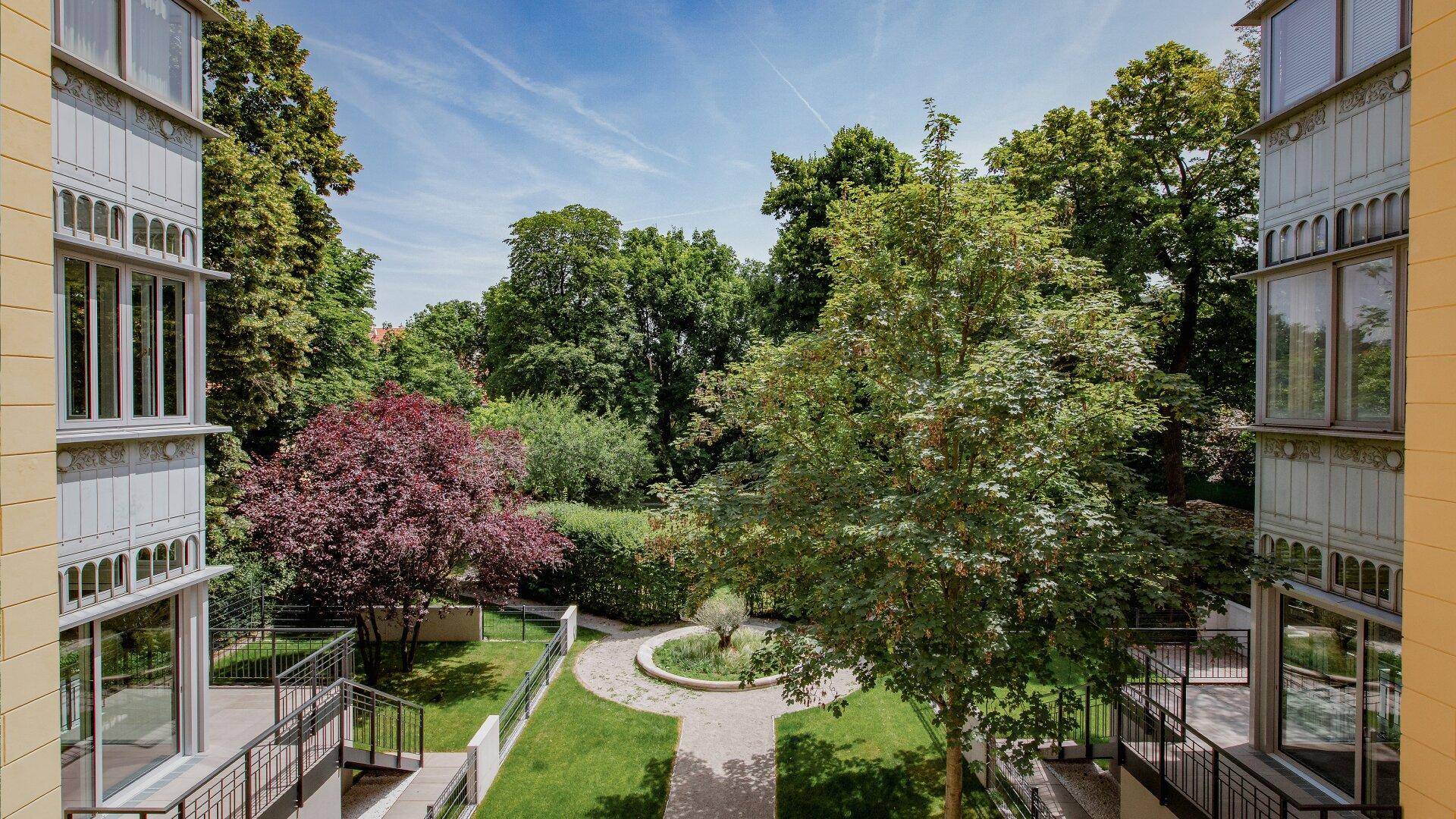 Blick auf den gepflegten Innenhof mit üppiger Vegetation und Bäumen unter blauem Himmel.