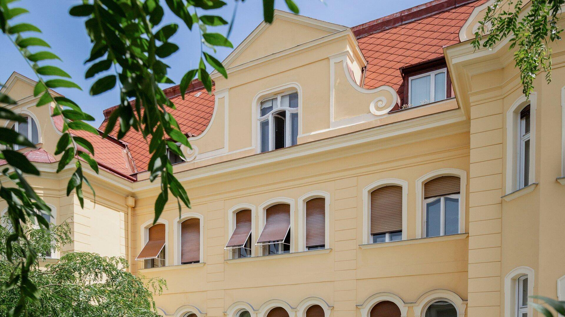 Seitenansicht der historischen Fassade mit roten Ziegeldächern und geöffneten Rollläden.
