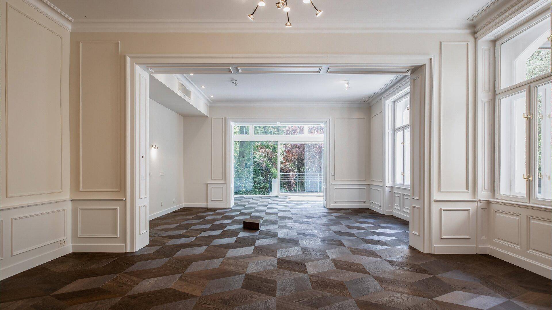 Geräumiger Wohnbereich mit elegantem Parkettboden, hohen Decken und großen Fenstern zum Garten.