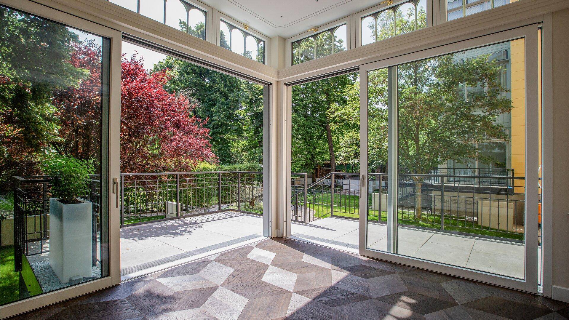 Heller Wintergarten mit großen Schiebetüren, Parkettboden und direktem Zugang zum Garten.
