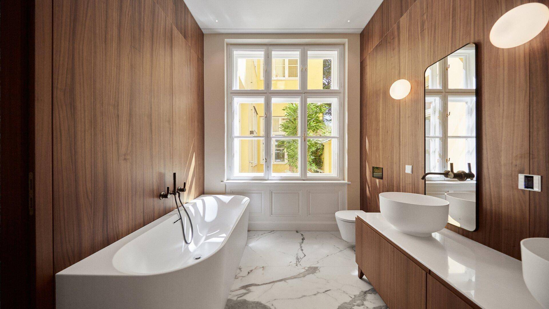 Elegantes Badezimmer mit freistehender Badewanne, Holzverkleidung und großem Fenster.