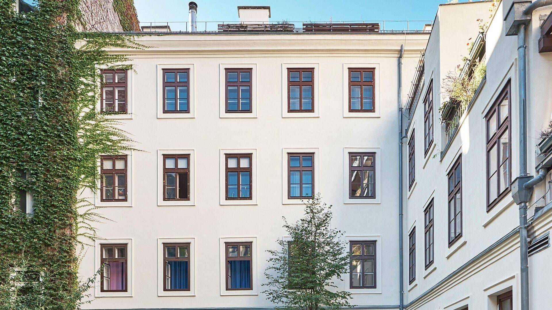 Innenhofansicht eines Wohngebäudes mit grüner Bepflanzung an der Fassade.