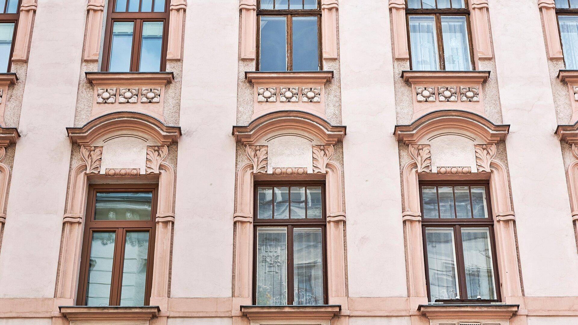 Detailaufnahme der reich verzierten Fenster und der historischen Fassade eines Altbaus.