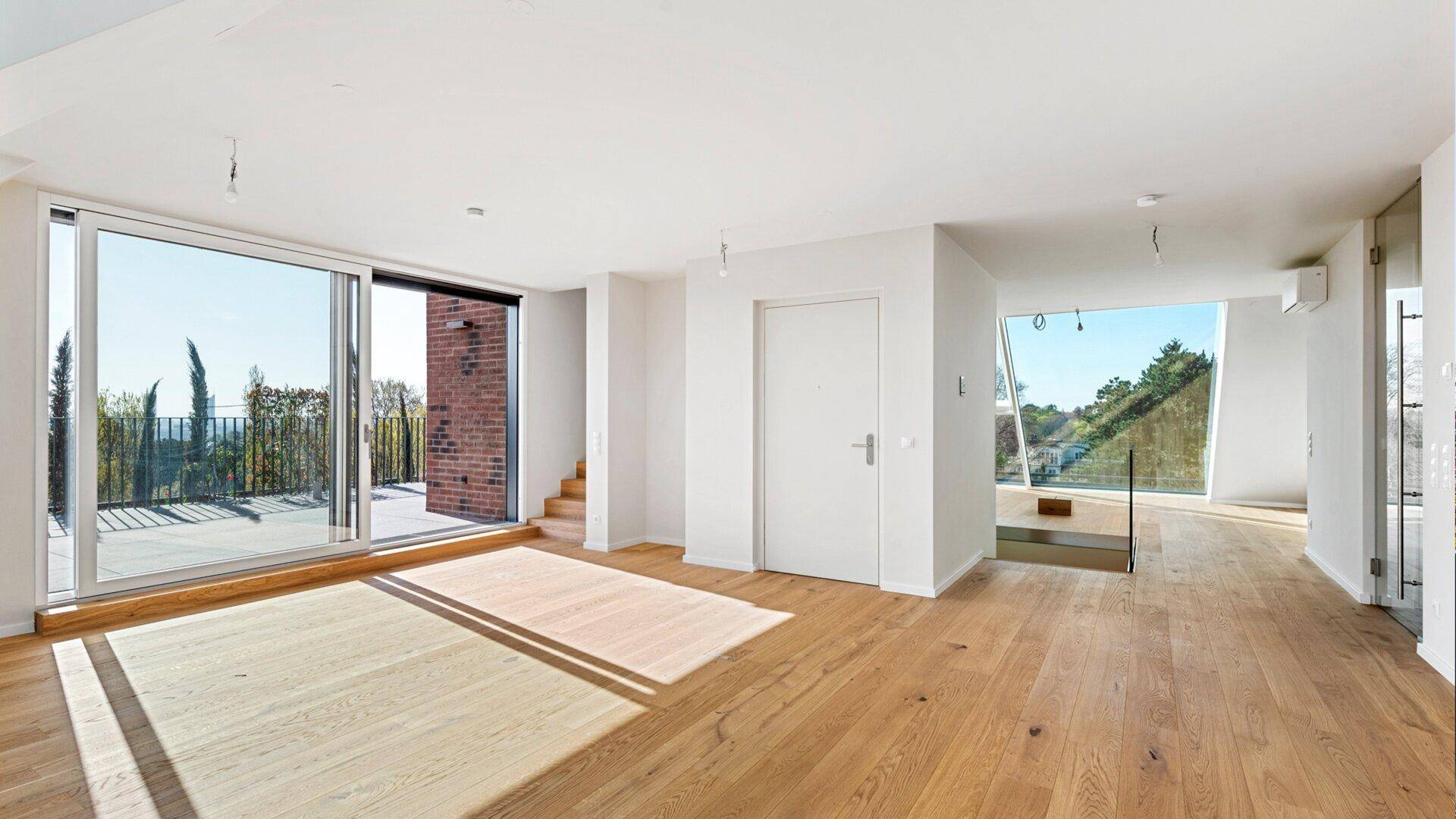 Geräumiges, lichtdurchflutetes Wohnzimmer mit Holzboden, Terrassenzugang und offener Treppe.