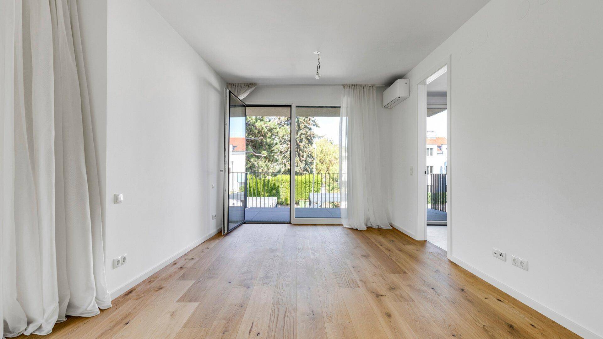 Helles Wohnzimmer mit Holzboden, Zugang zum Balkon und einer Klimaanlage für angenehmes Raumklima.