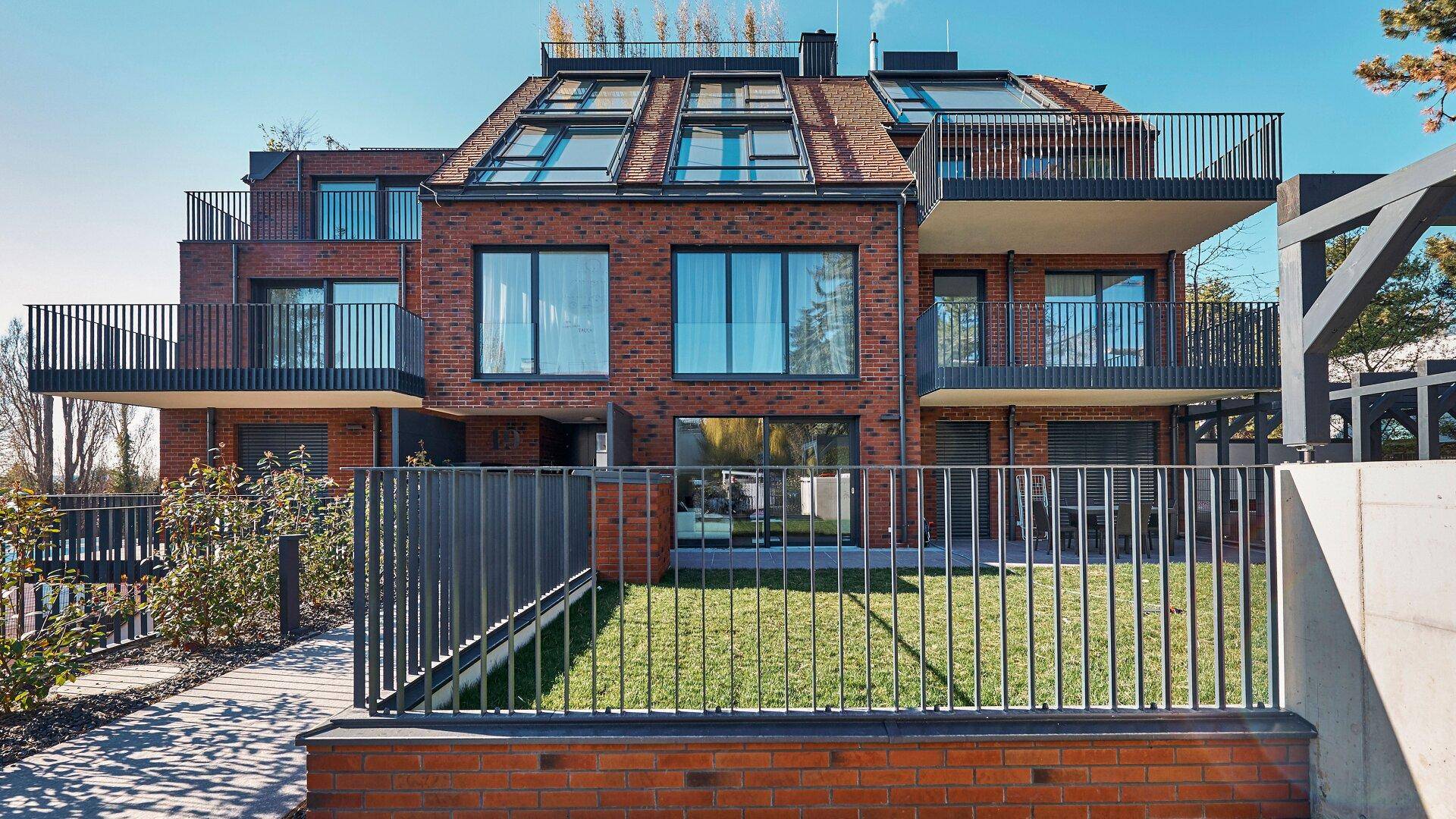 Moderne Wohnanlage mit roter Ziegelfassade, großen Fenstern und Balkonen.