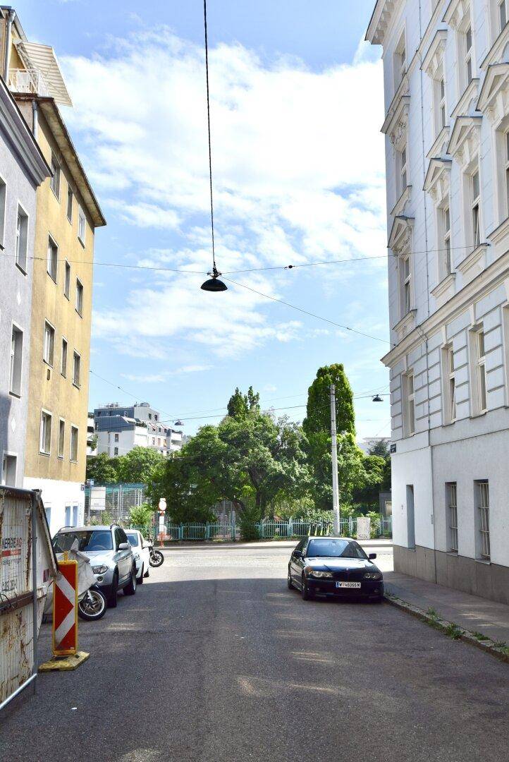 Ruhige Wohnstraße mit geparkten Autos und Bäumen im Hintergrund unter blauem Himmel.