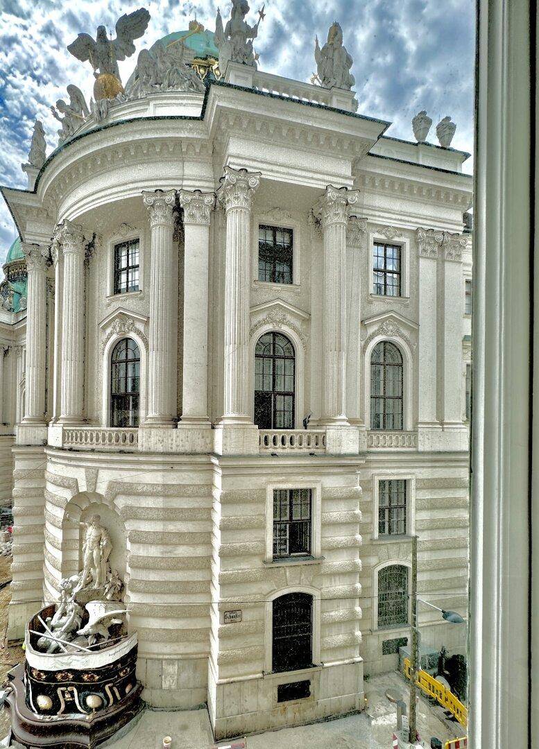 Ansicht eines prächtigen historischen Gebäudes mit Säulen und Balkonen, gesehen aus einem Fenster.