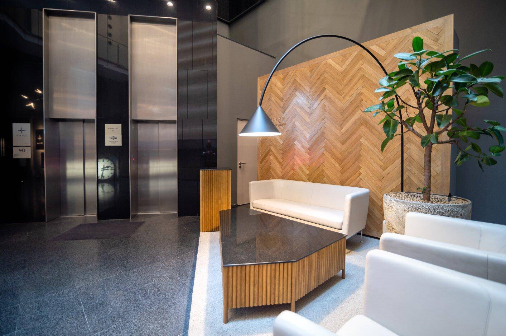 Elegante Lobby mit Aufzügen, bequemen Sitzgelegenheiten und einer dekorativen Holzwand.