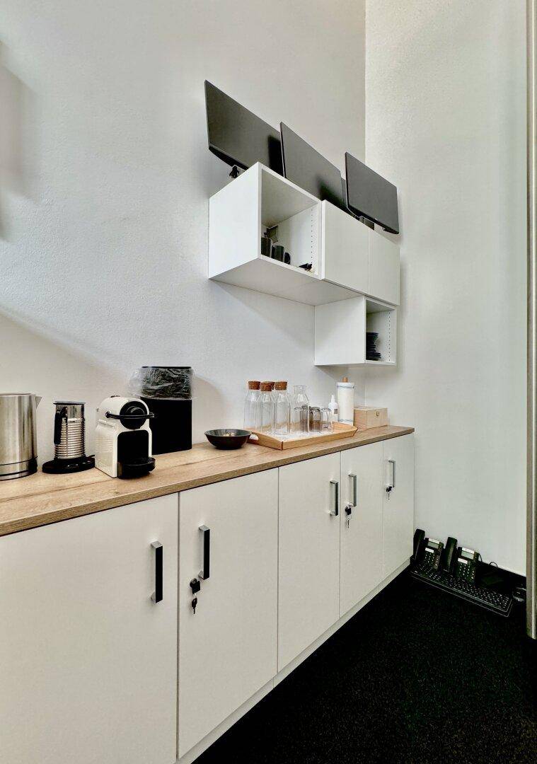 Kleine Küchenzeile mit Holzarbeitsplatte, weißen Schränken und Kaffeemaschine.