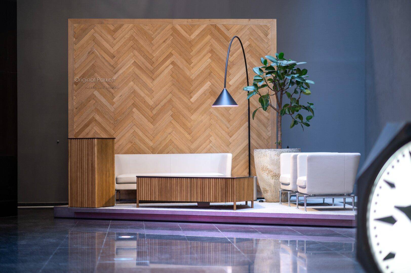 Gemütlicher Wartebereich mit Holzvertäfelung, bequemen Sofas und einer großen Pflanze.