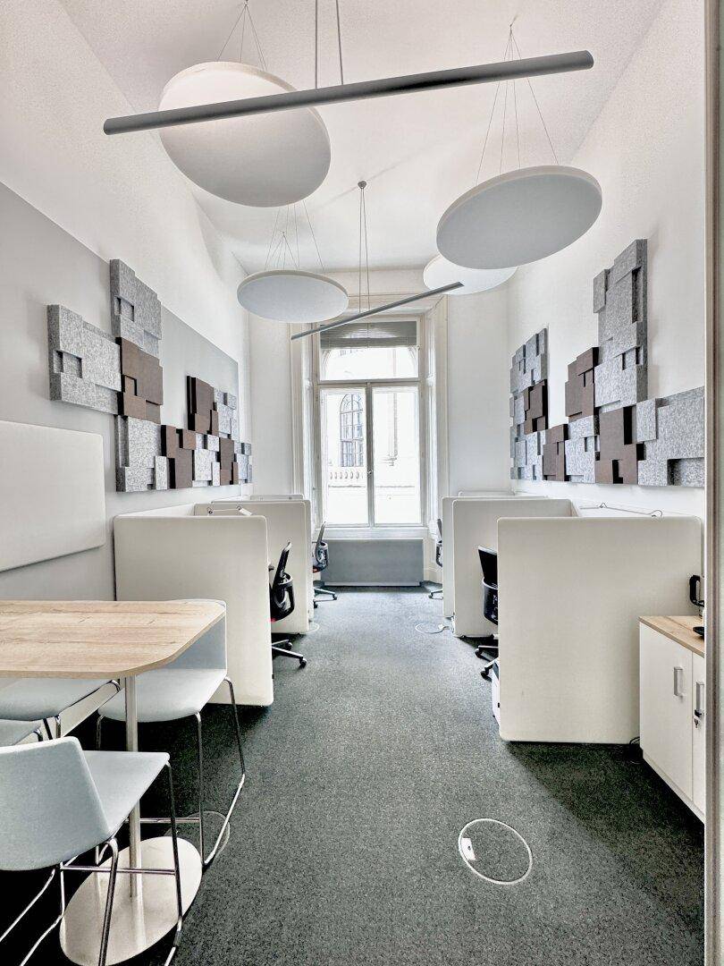Helles Büro mit Arbeitsplätzen, schallabsorbierenden Elementen und Blick auf die Stadt durch das Fenster.