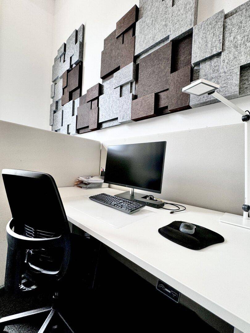 Detailansicht eines modernen Schreibtisches mit Computerbildschirm und ergonomischem Stuhl.