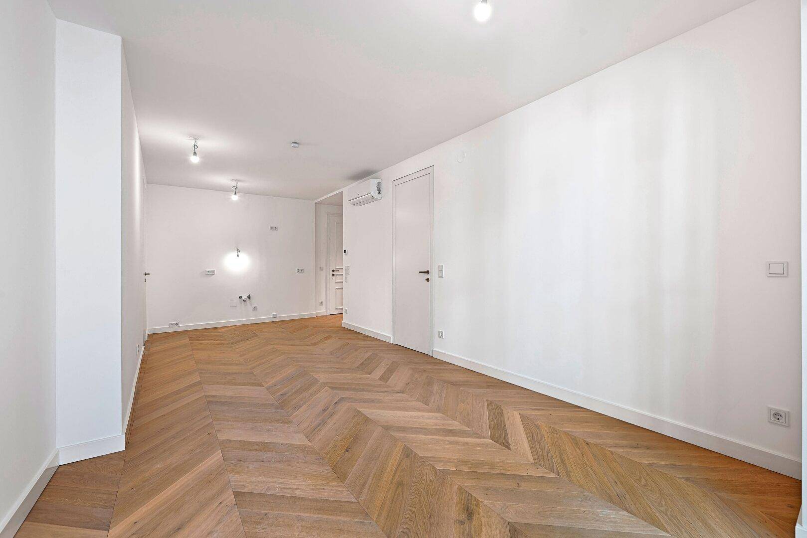 Heller, leerer Raum mit Fischgrätparkett und modernen Wandanschlüssen.