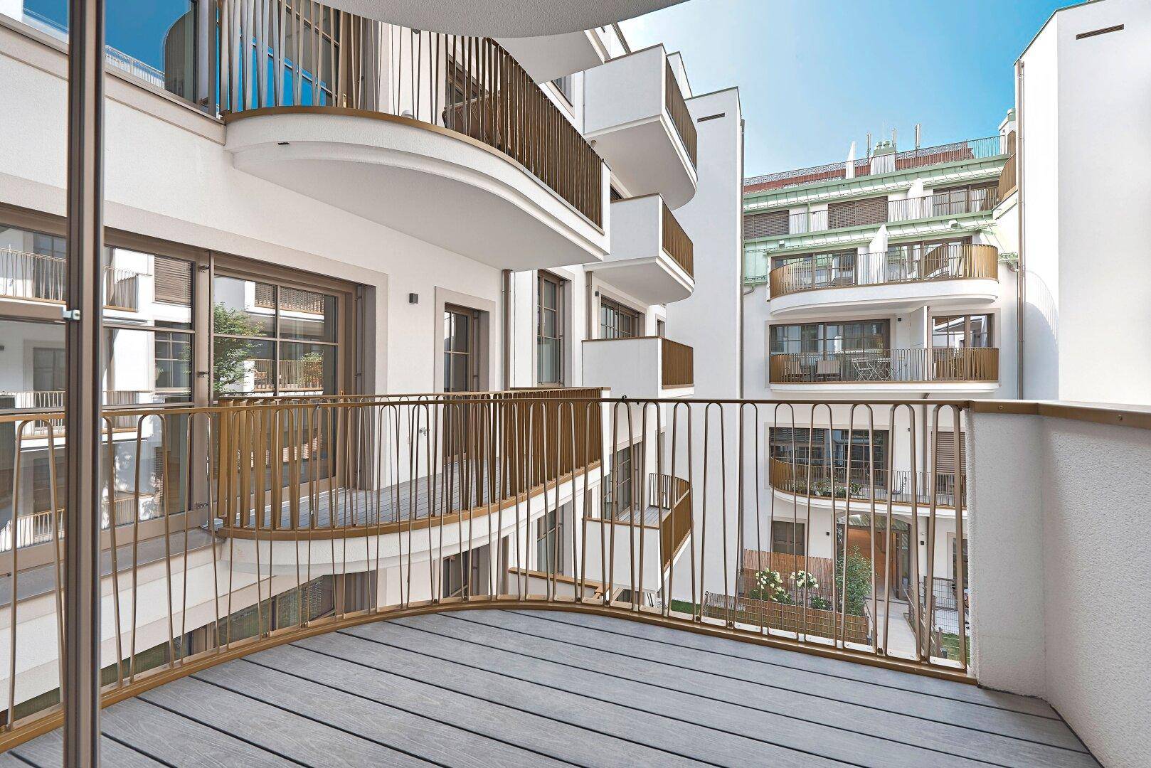 Moderner Balkon mit Holzdeck und elegantem Metallgeländer, umgeben von weiteren Balkonen.