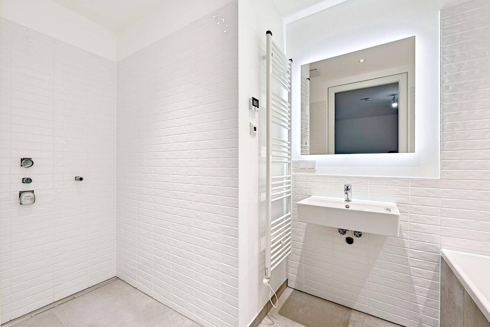 Modernes Badezimmer mit weißen Fliesen, Einzelwaschbecken, beheiztem Handtuchhalter und Duschbereich.