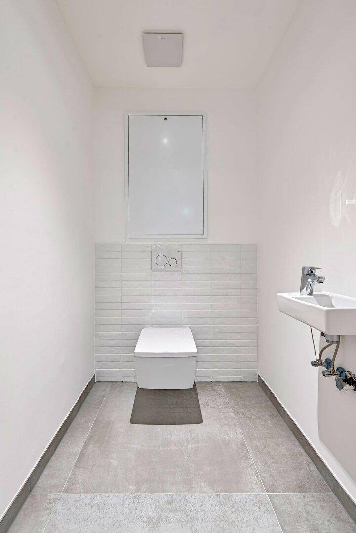 Modernes Gäste-WC mit wandhängender Toilette, kleinem Waschbecken und grauen Bodenfliesen.