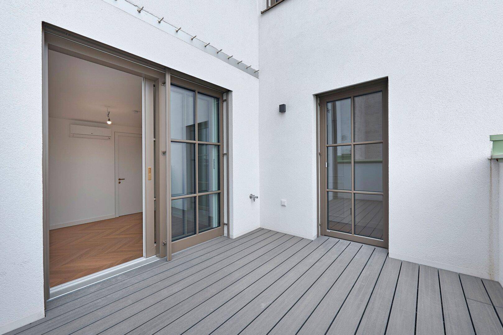Kleiner Balkon mit Holzoptik-Bodenbelag und Zugang zu einem hellen Innenraum.