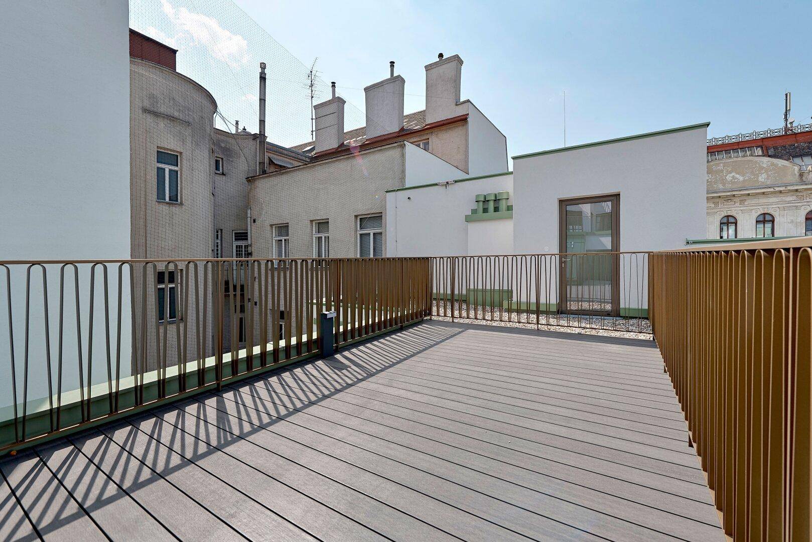 Geräumige Dachterrasse mit Holzoptik-Bodenbelag und Blick auf die umliegenden Dächer.