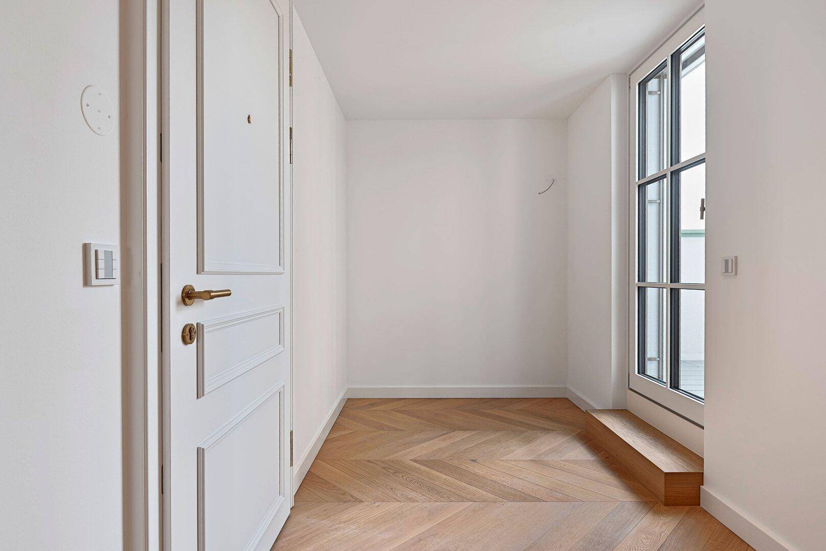 Heller Flur mit Fischgrätparkett und einer eleganten weißen Tür mit goldenem Griff.
