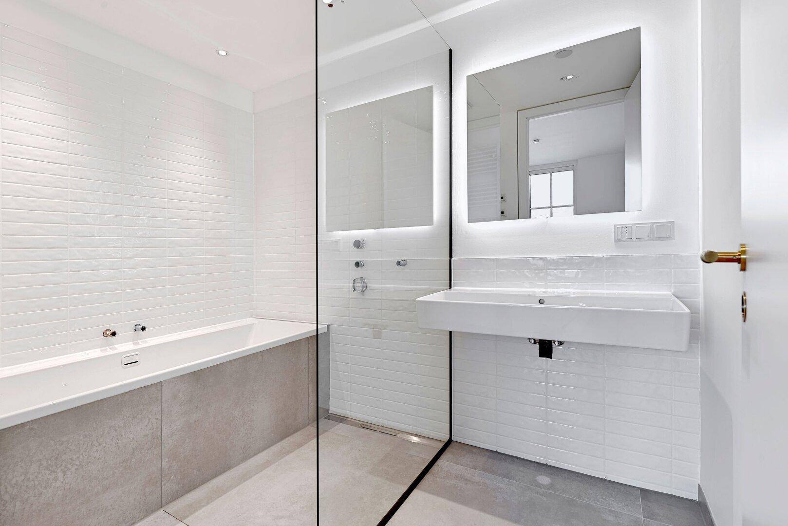 Modernes Badezimmer mit Badewanne, begehbarer Dusche und beleuchtetem Spiegel.