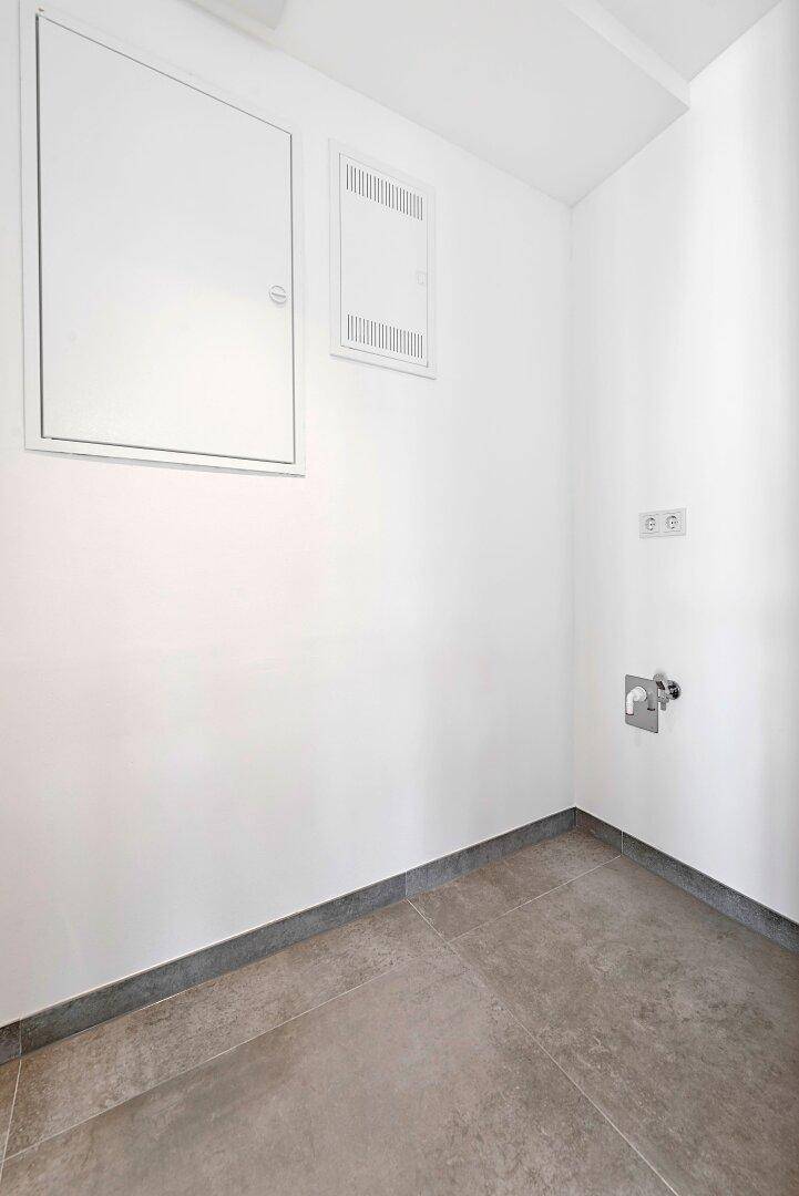 Leerer Hauswirtschaftsraum mit Fliesenboden und Anschlüssen für Waschmaschine.
