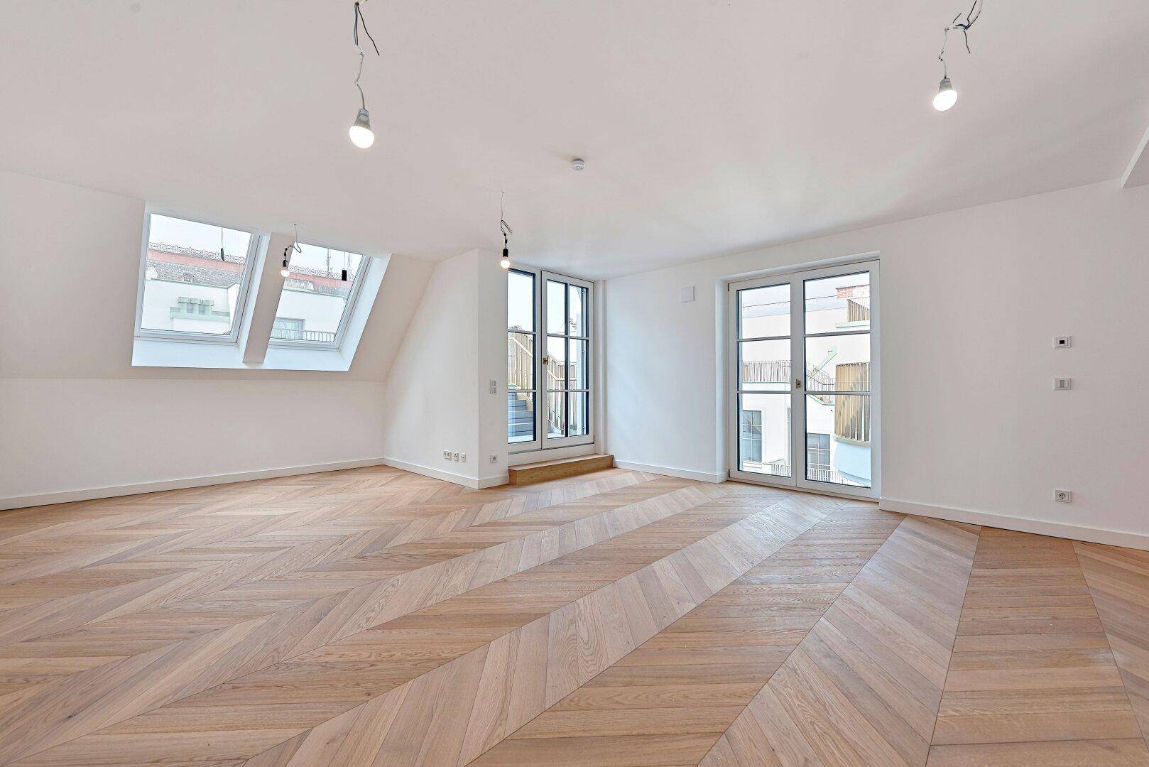 Helles, geräumiges Zimmer mit modernem Fischgrätparkett, Dachschrägen und Zugang zu einem französischen Balkon.